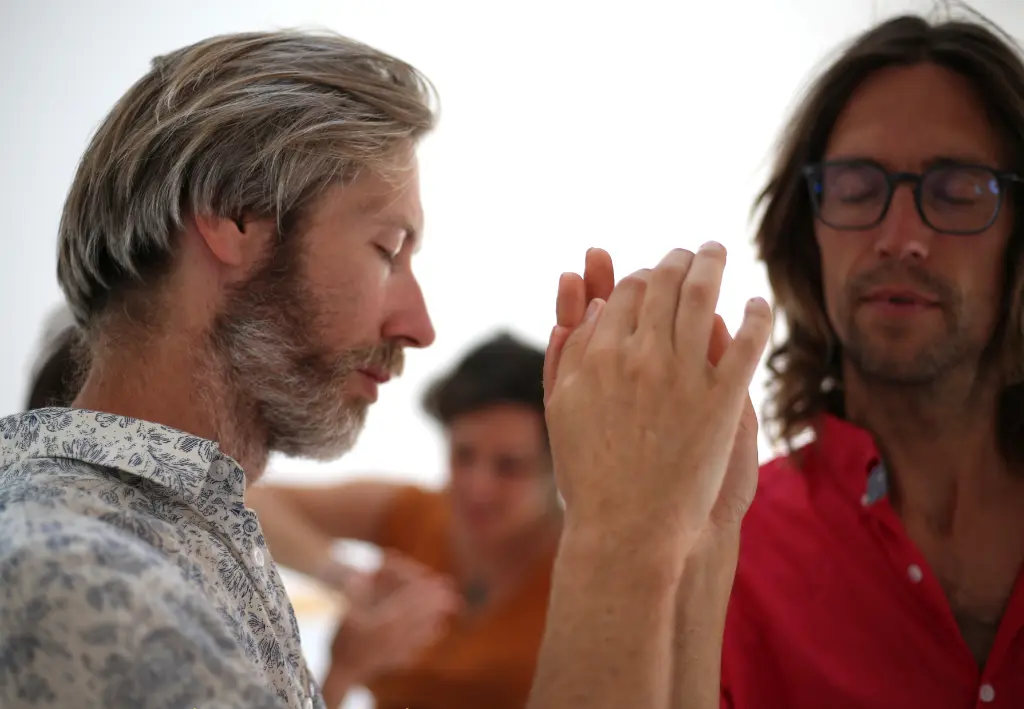 Deux danseurs, les yeux fermés, partagent avec sensibilité une danse avec leurs index réunis lors d’une proposition d’une séance de Biodanza